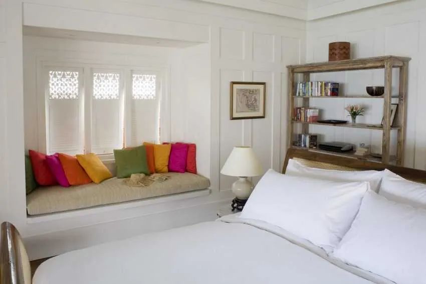 Открытый стеллаж за кроватью и диван-подоконник в маленькой спальне
